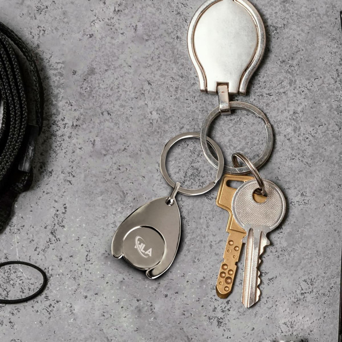 A silver teardrop-shaped trolley coin keyring attached to metal keyrings and keys on a textured surface.
