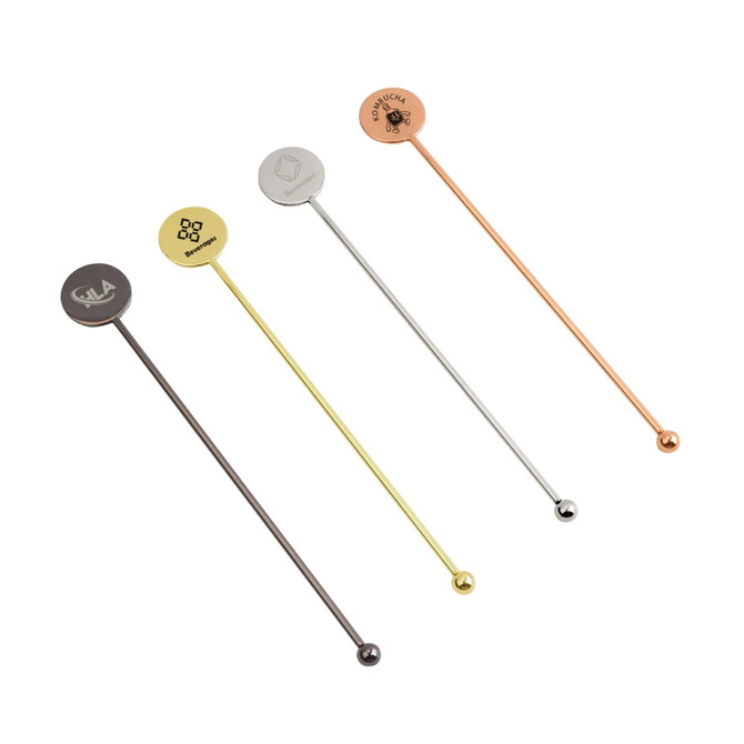 A set of four stainless steel cocktail drink stirrers in gold, silver, copper, and black finishes, each with a logo.