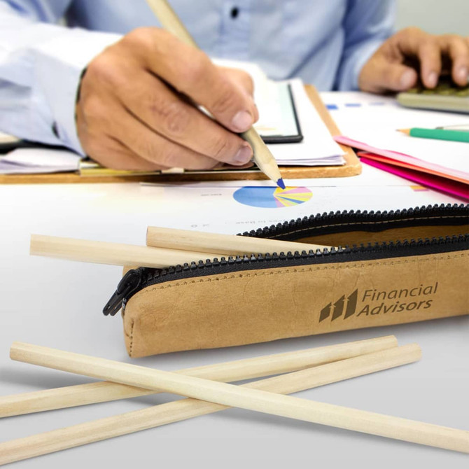 A pencil case in a tan colour with wooden pencils scattered nearby and a person drawing on a document.