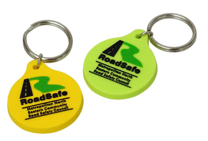 Two custom PVC keyrings in yellow and green, each featuring a logo and attached to a metal key ring.