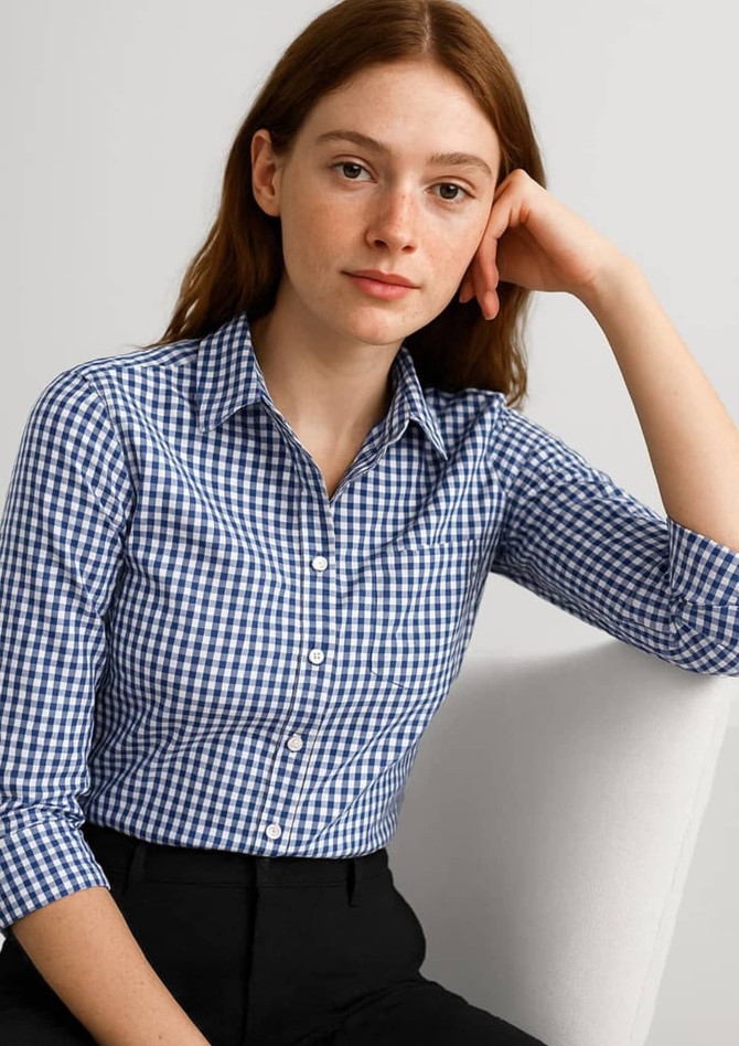 A woman models a blue and white gingham button-up shirt with 3/4 sleeves. The shirt has a collar and buttons.