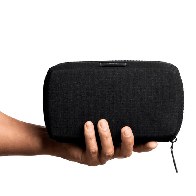 A black tech kit held in a hand, featuring a zip closure and a branding logo.