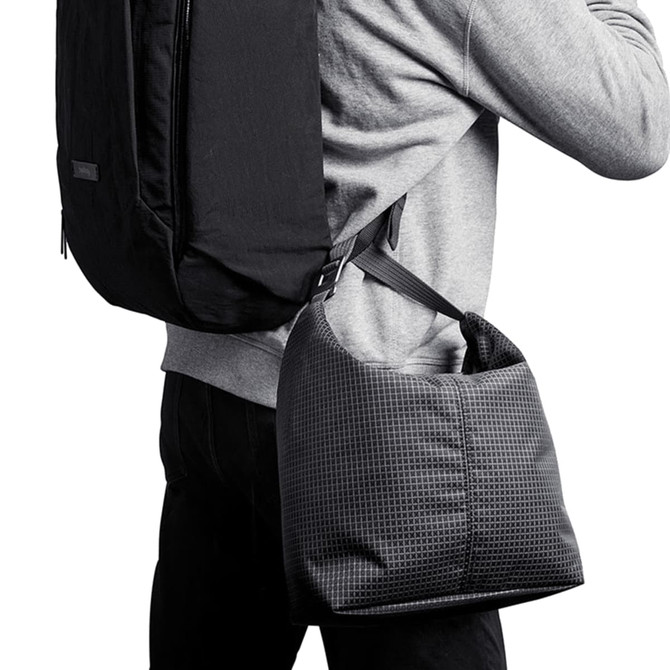 A cooler bag in a grid pattern, featuring a shoulder strap, being carried on the side of a person with a backpack.