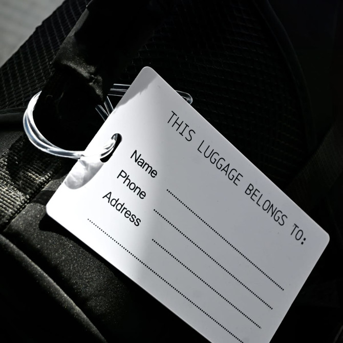 A large black luggage tag featuring a white identification label for name, phone, and address.