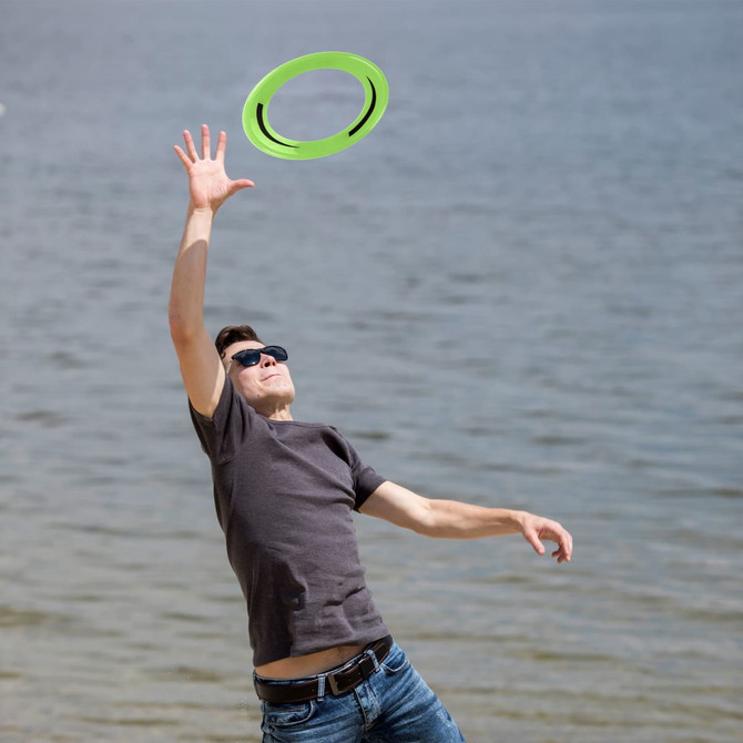 A man in sunglasses reaches for a green frisbee by the water. The background features a serene beach scene.
