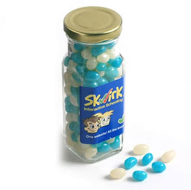 A tall glass jar filled with blue and white mini jelly beans, with a gold lid and a logo on the front.
