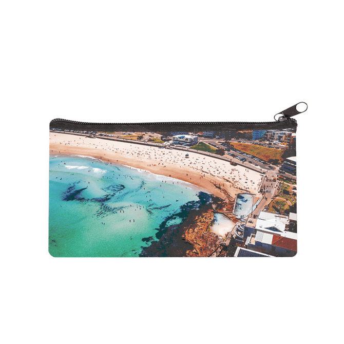 A large neoprene pencil case featuring a vibrant coastal scene with shades of blue and sandy beach. It has a zippered closure.
