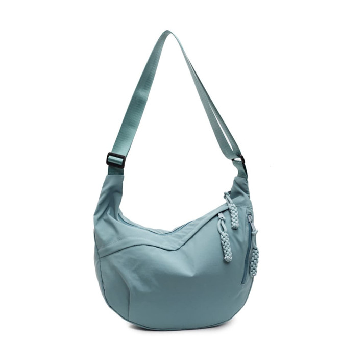 A light blue Dumpling Crossbody Bag featuring a curved shape and adjustable strap with decorative pulls.