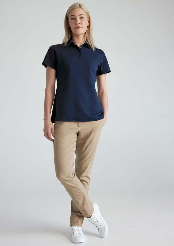 A woman in a navy short sleeve polo shirt paired with khaki trousers and white sneakers. The shirt has a logo.
