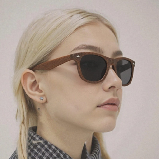 Brown sunglasses made from coffee fibre, featuring dark lenses and a minimalist design. The model has light hair.