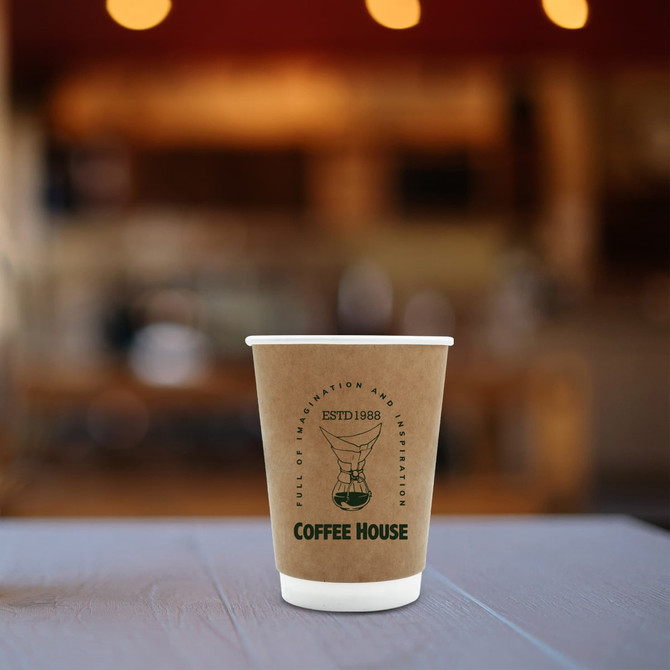 A kraft paper cup in brown and white, featuring a logo, set against a blurred café background.