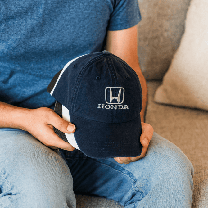 A navy blue denim cotton baseball cap with a logo, held by a person wearing a blue shirt, sitting on a couch.
