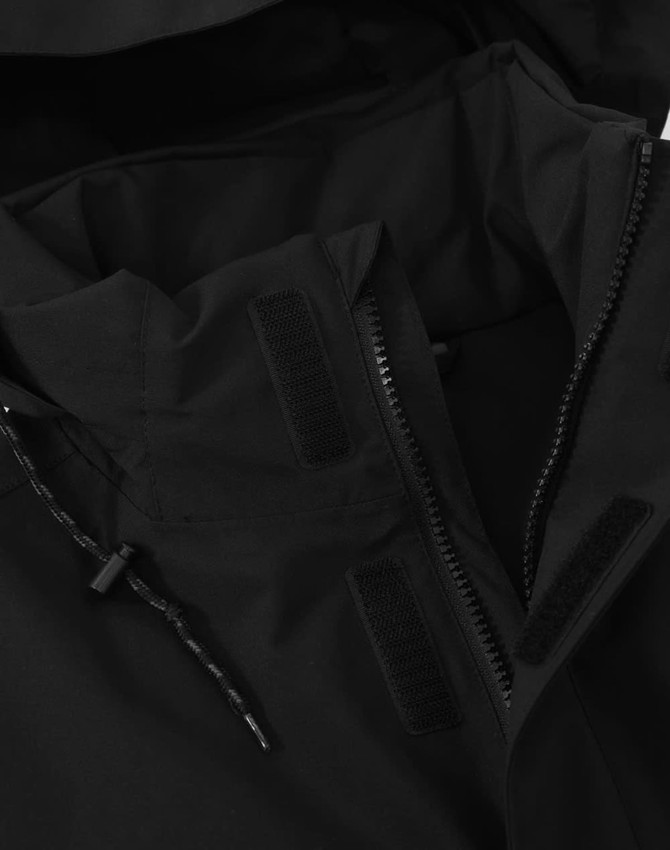 A black unisex quilted waterproof jacket featuring a high collar and zip closure, with velcro detailing.