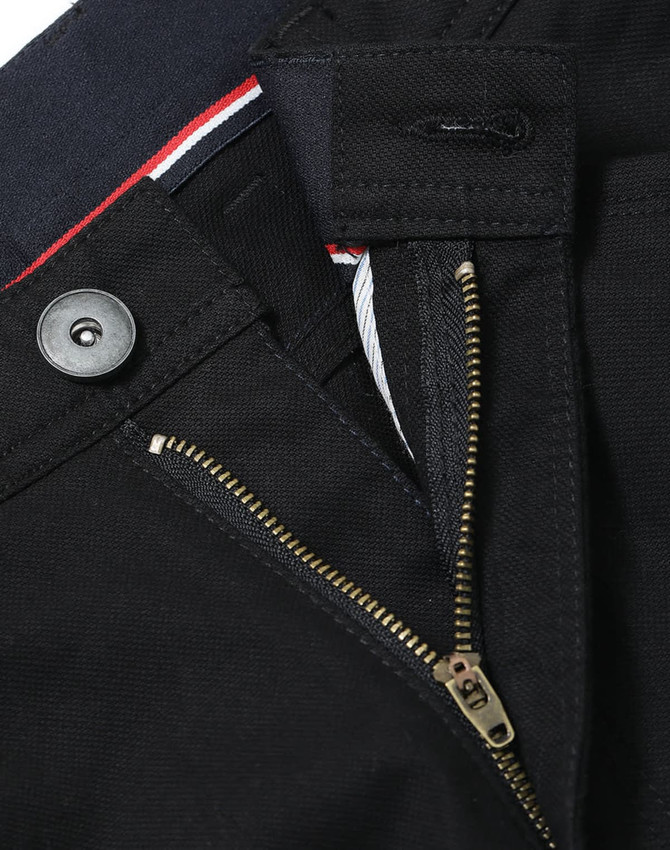 A close-up of black ladies' chino pants, featuring a zip fly, button closure, and a branded label.