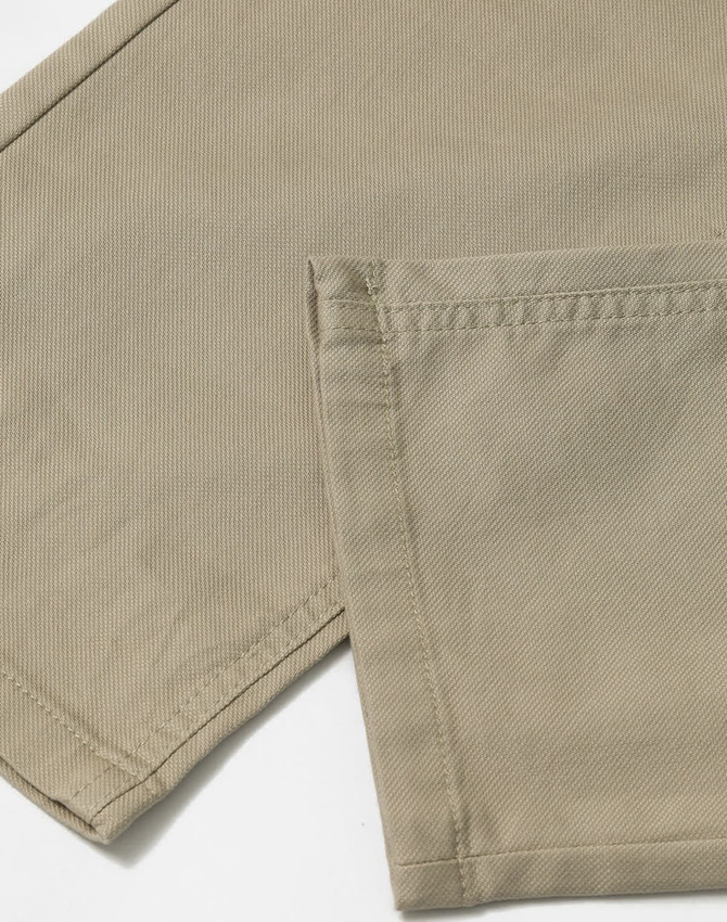 A close-up of khaki chino pants, highlighting the fabric and stitched hem. The image features a logo or branding detail.