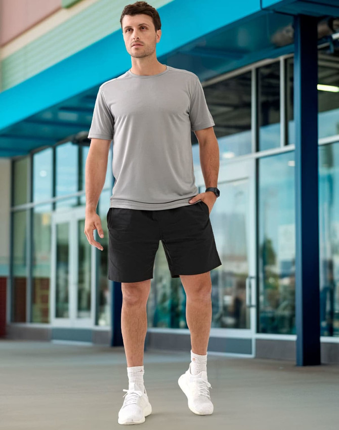 A man is wearing unisex grey mercerised cotton shorts with a matching grey shirt and white sneakers in an outdoor setting.