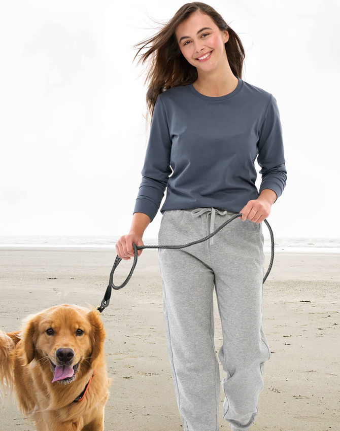 A woman walks a golden retriever on the beach, wearing a dark grey long-sleeve tee and grey sweatpants.