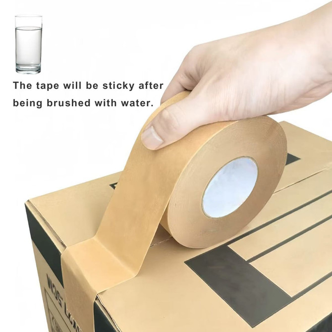 A hand holds a roll of brown water-activated gummed kraft paper tape above a cardboard box. The tape has a circular inner core.