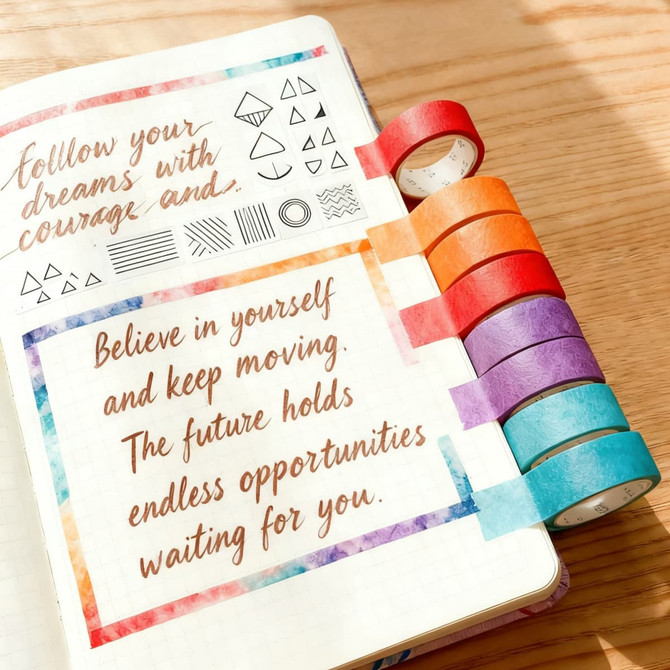 Washi tape in various colours—red, orange, purple, and blue—adorns the edge of a notebook with motivational quotes.
