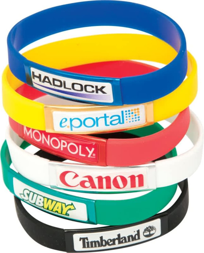 A stack of silicone wristbands in various colours, featuring different logos and branding on each band.