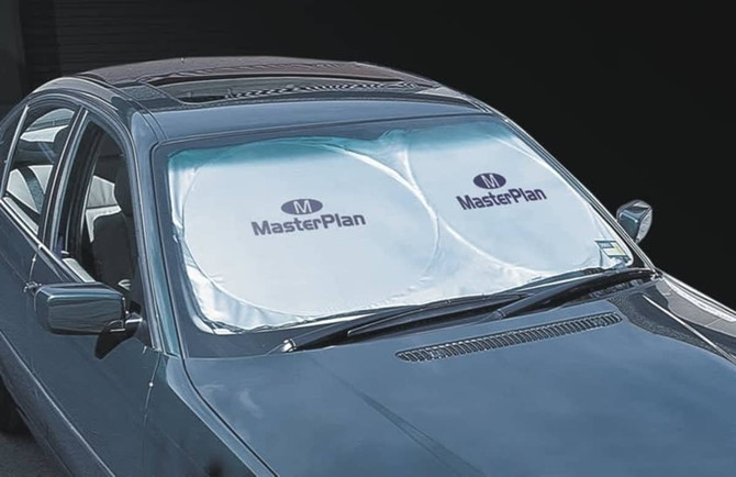 A silver sunshade with circular cutouts is placed on a car's windscreen, featuring a logo.