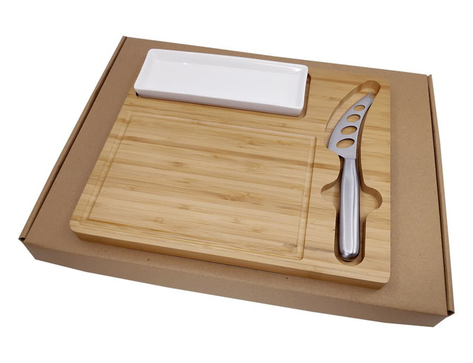 A bamboo cheese board set with a stainless steel knife and a white serving dish in a cardboard box.