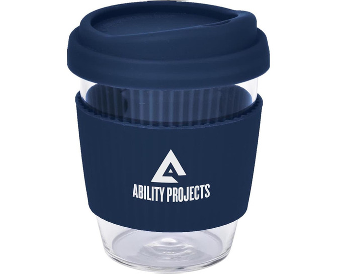 A reusable coffee cup in clear glass with a navy blue silicone lid and band, featuring a logo.