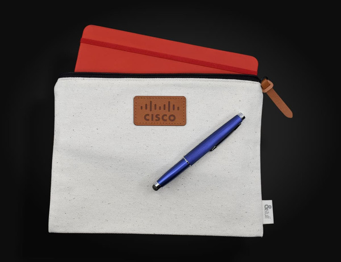 A cream conference bag featuring a brown logo patch, a red tablet cover, and a blue pen.