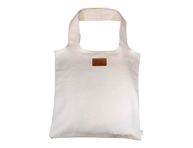 A cream-coloured tote bag made of calico, featuring a logo patch on the front.
