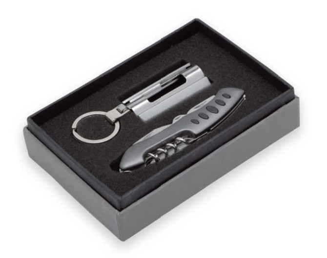 A black gift box containing a silver multi-tool and keyring accessory, presented on a plush interior.