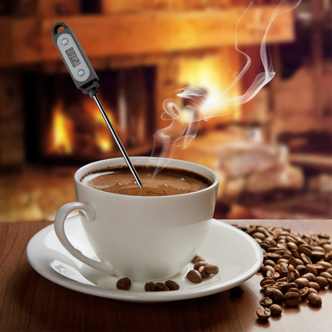 A white cup of coffee with steam rising, featuring a silver and black meat thermometer inserted into it.