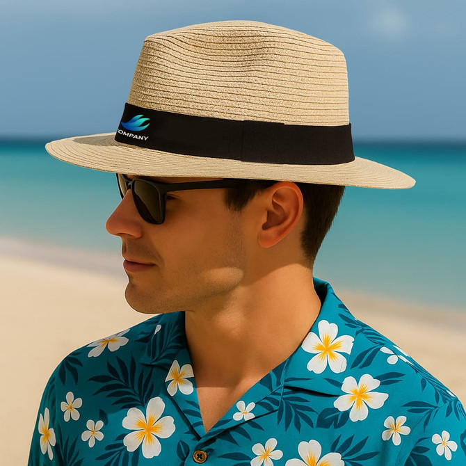 A sun hat in a light beige colour with a black band, worn by a man in a floral patterned shirt by the beach.