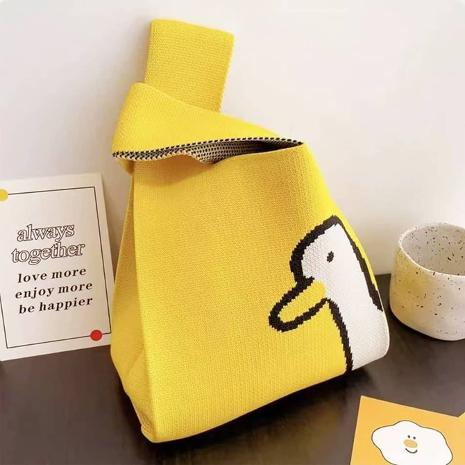 A yellow knitted handbag featuring a duck design, accompanied by a small cup and promotional card.
