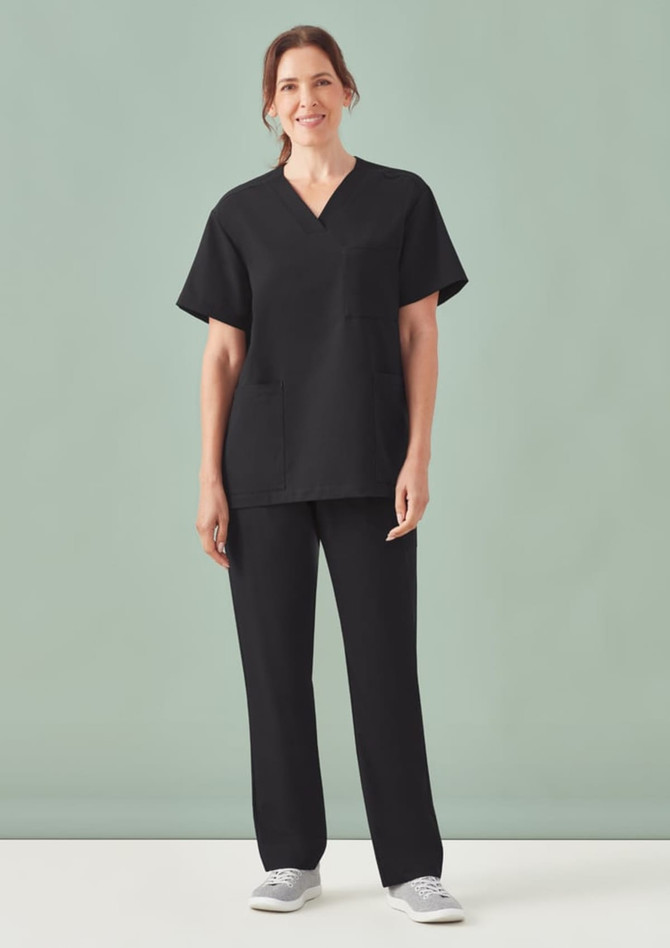 A woman wearing a black unisex pulse V-neck scrub top with matching pants, set against a light green background.