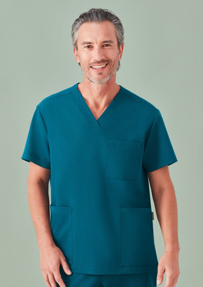 A unisex pulse v-neck scrub top in teal, featuring a pocket and a logo. The model is smiling.