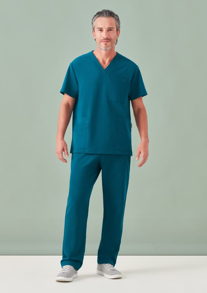 A male model wearing a teal unisex V-neck scrub top and matching pants, posing against a neutral background.