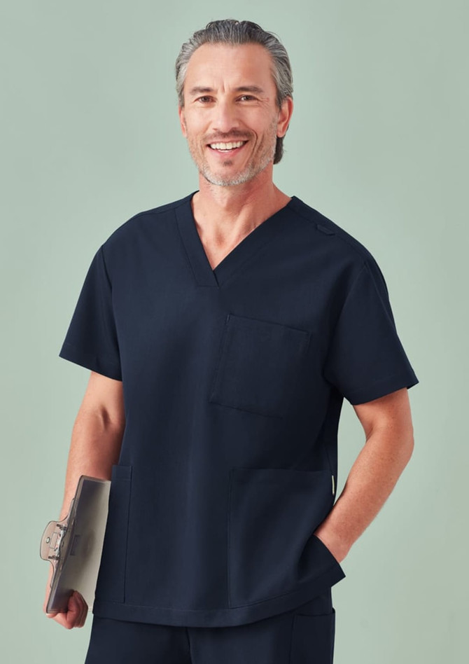 A unisex navy V-neck scrub top with a pocket, worn by a smiling model holding a clip folder.