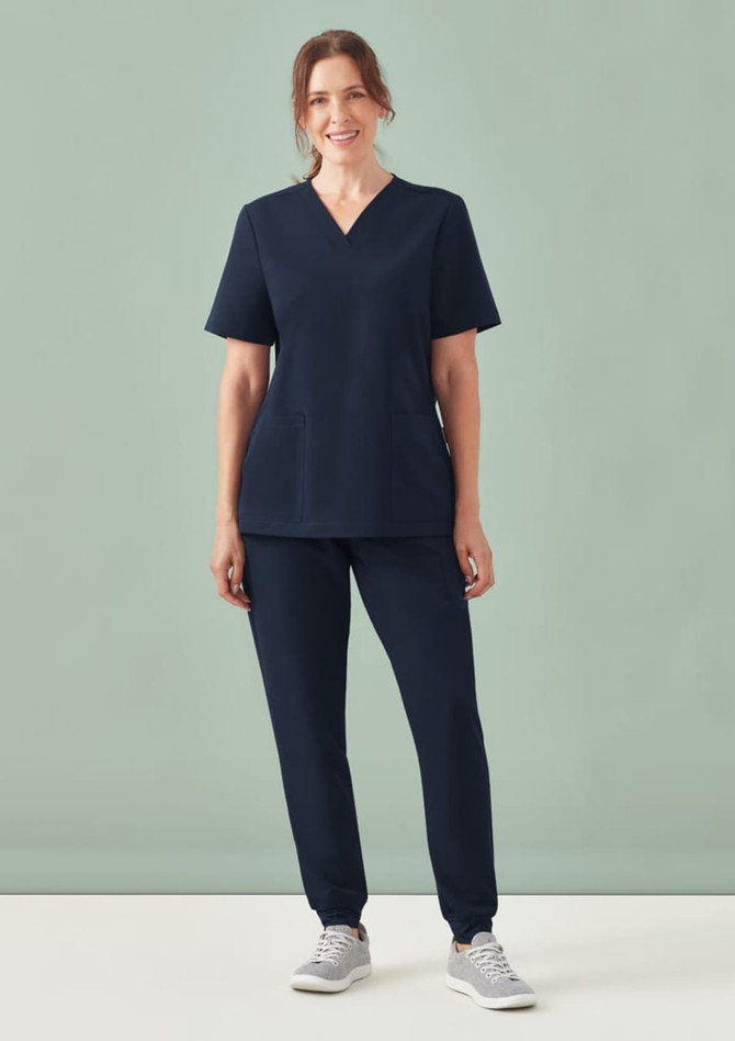A navy women's V-neck scrub top paired with matching pants, modelled on a woman standing against a light green background.