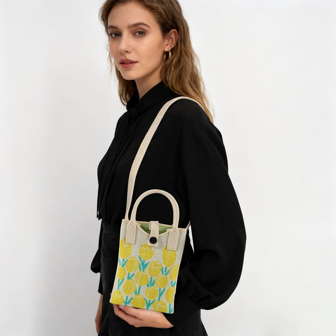A knitted crossbody bag in yellow and blue with a handle, displayed by a model wearing a black shirt.
