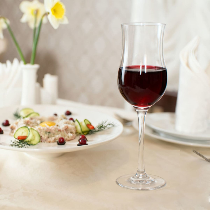 A tulip-shaped wine glass filled with red wine, set beside a plated dish with garnishes, on a elegantly arranged table.