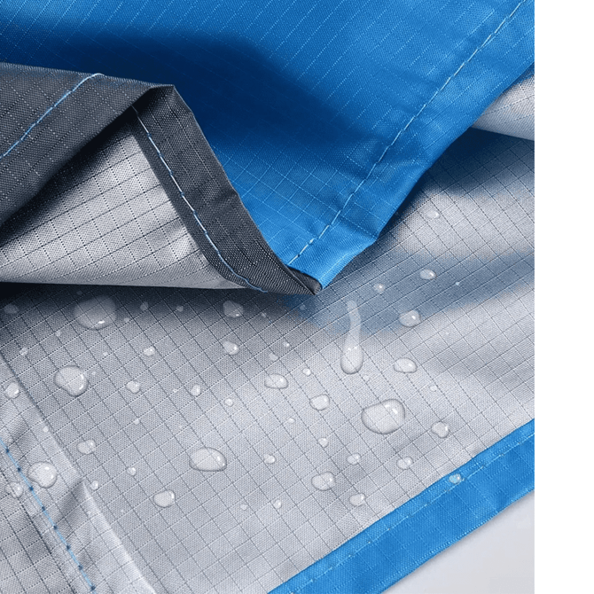 A close-up of a blue polyester picnic blanket featuring a water-resistant underside with droplets. It has a logo.