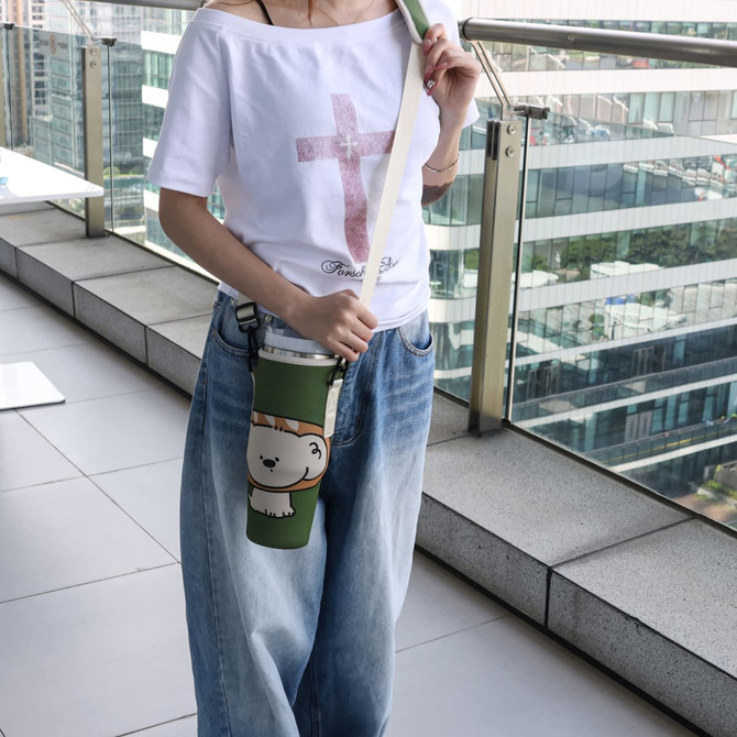 A drink bottle carrier bag in green, featuring a logo, being held by a person wearing casual attire.