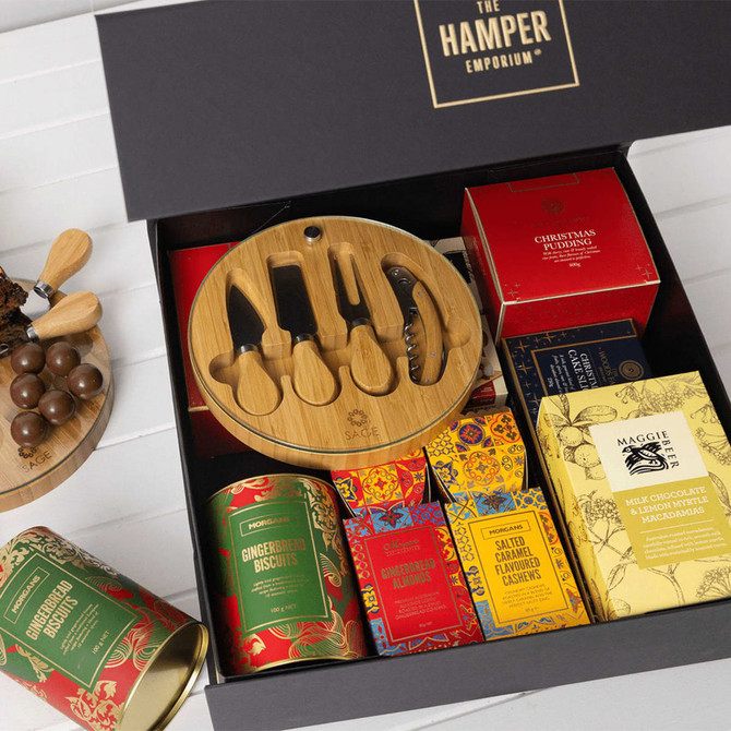 A gift pack featuring a bamboo board with knives and assorted gourmet treats in vibrant packaging. Contains a logo.
