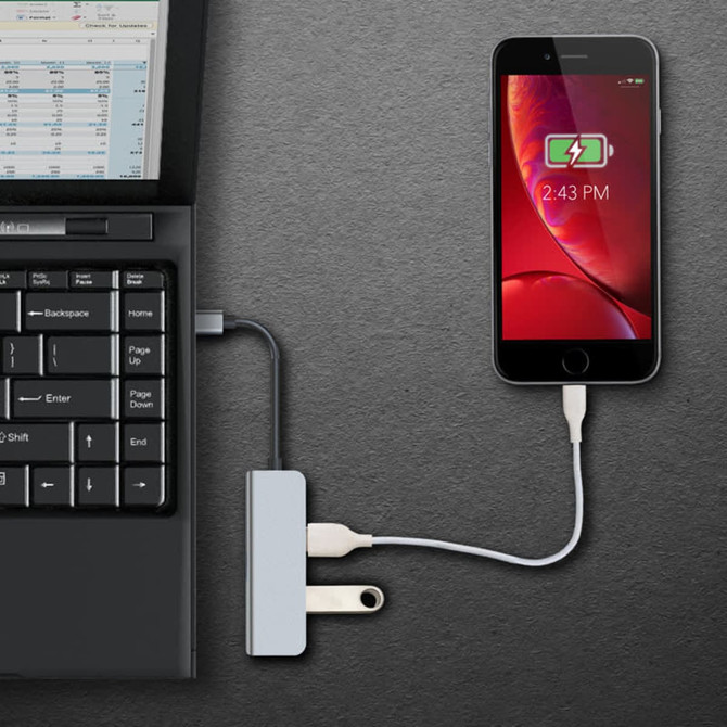 A Type-C hub in grey connecting a laptop to a phone, with a visible power source and a charging indicator on the phone.