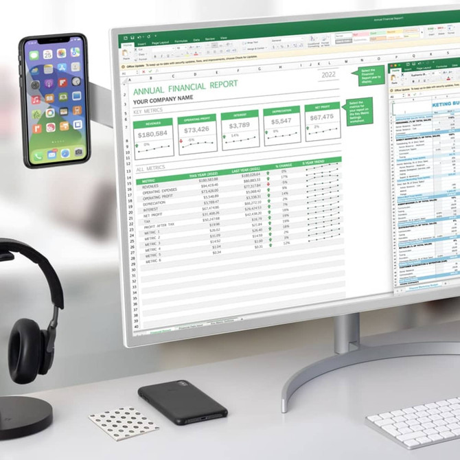 A laptop extension arm in black holds a smartphone above a computer displaying a financial report, with headphones nearby.