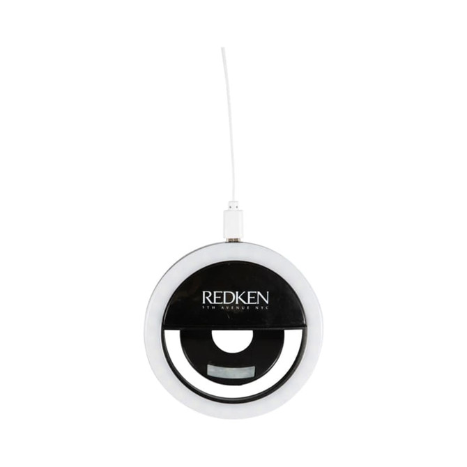 A round, white LED selfie light with a black centre and a white charging cable, featuring a logo.