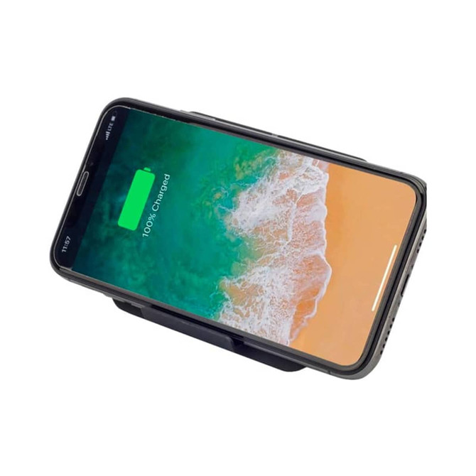 A black wireless charger stand with a phone displaying a fully charged battery on a beach-themed background.