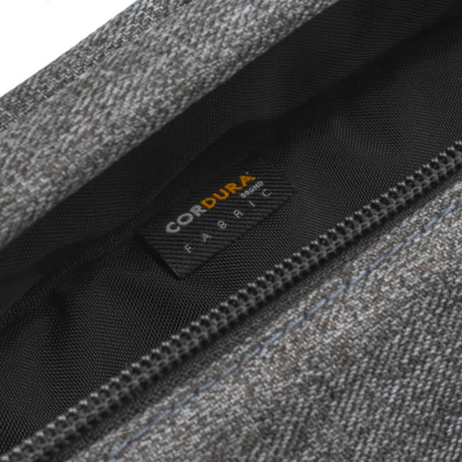 A close-up of a grey fabric bag showing a hidden zip and tag, featuring a logo on the inner lining.
