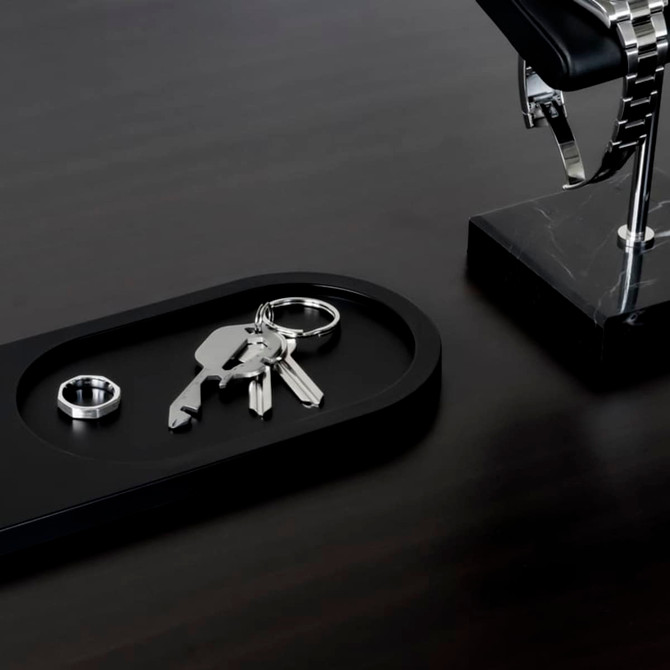 A sleek metallic multi-tool resting on a black tray alongside keys and a ring, set on a polished dark surface.