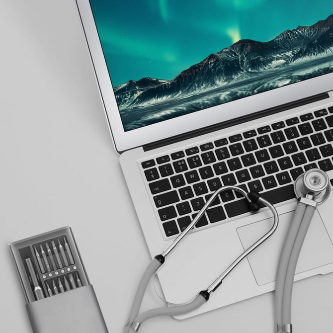 A precision tool kit in a silver case, featuring multiple screwdrivers, beside a laptop and stethoscope.